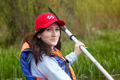 SOFTSWISS employee rowing a kayak, wearing a red cap with the company logo.