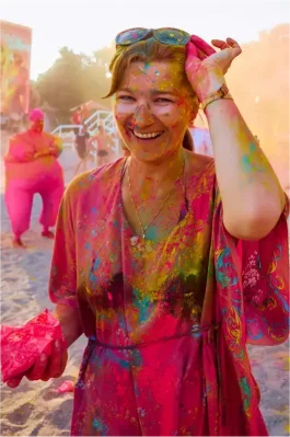 A girl smiling and covered in vibrant colored powder during a festival celebration.