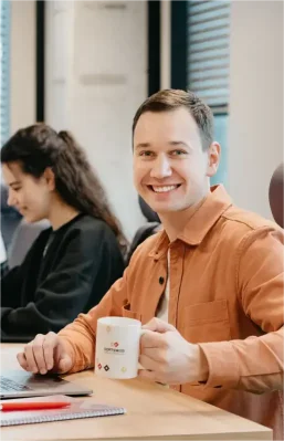 SOFTSWISS employee smiling while holding a branded mug during work at the office.