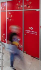 SOFTSWISS-branded red wall with company logo and a blurred figure walking past