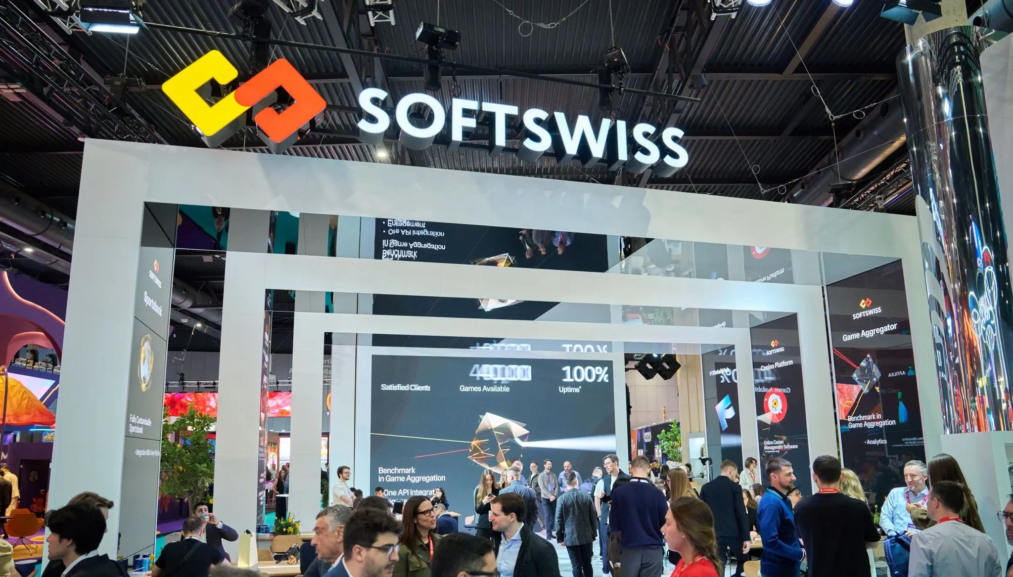 SOFTSWISS logo, white and transparent booth, people at the booth