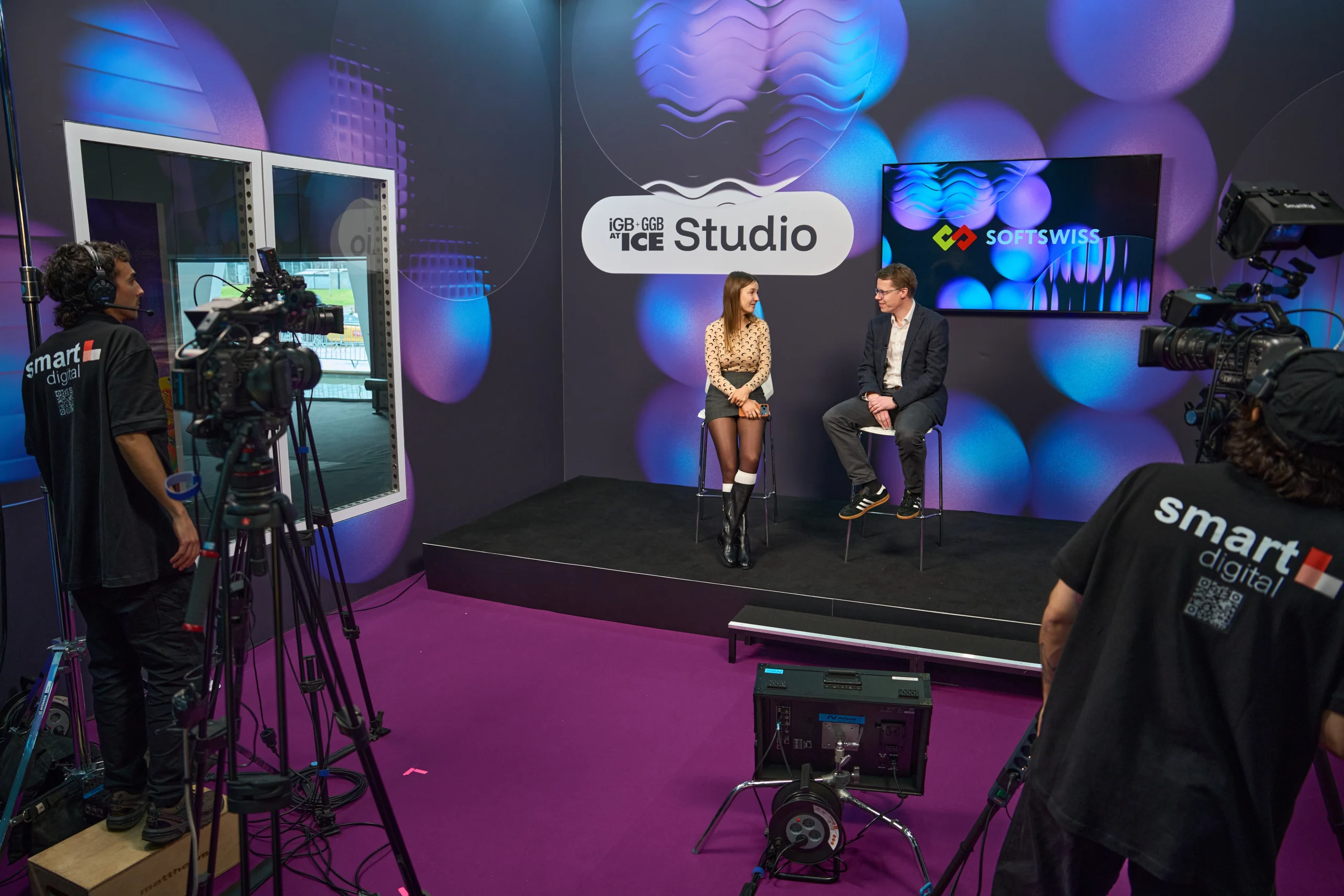 Olga Resiga and Ronnie Whelan, seat an the chairs, black and purple background and carpet