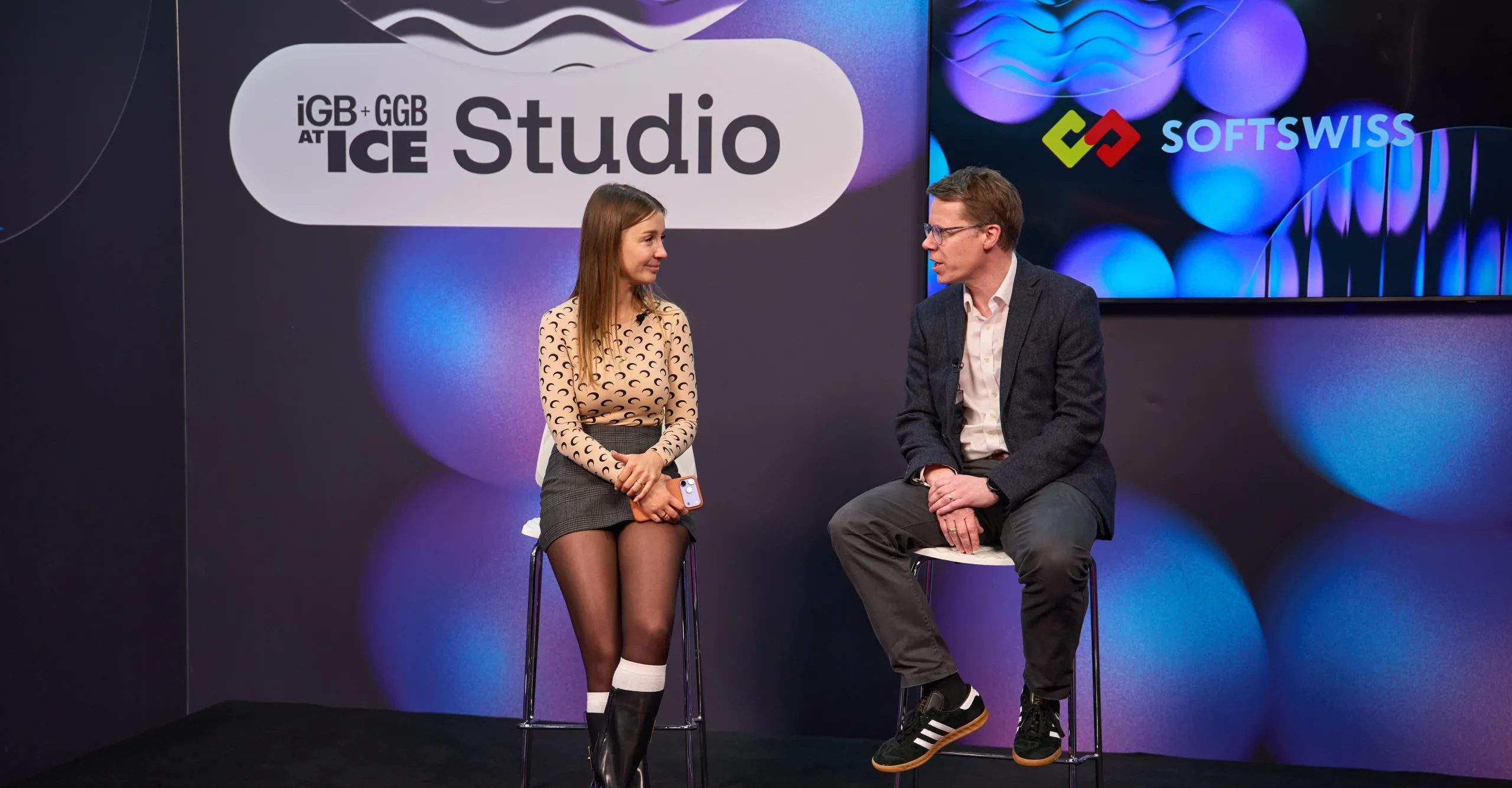 Olga Resiga and Ronnie Whelan, seat an the chairs, black and purple background