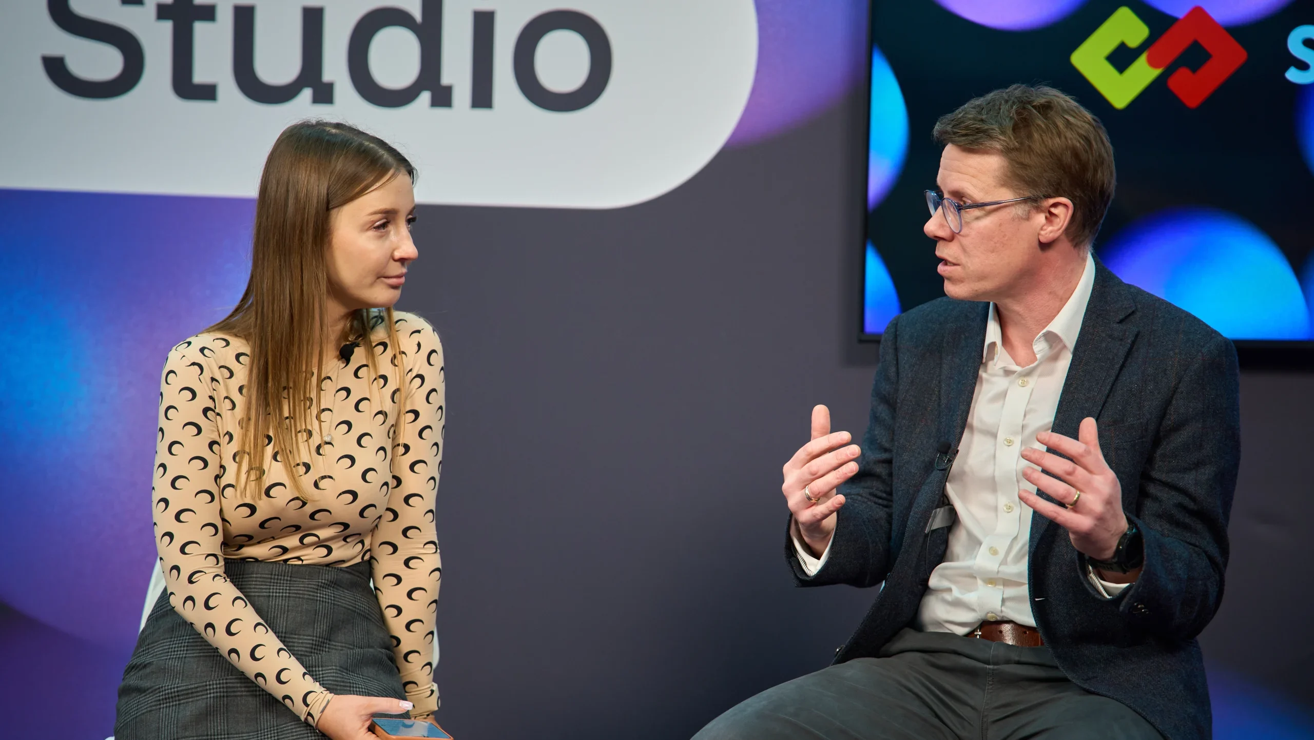 Olga Resiga and Ronnie Whelan, seat an the chairs, black and purple background