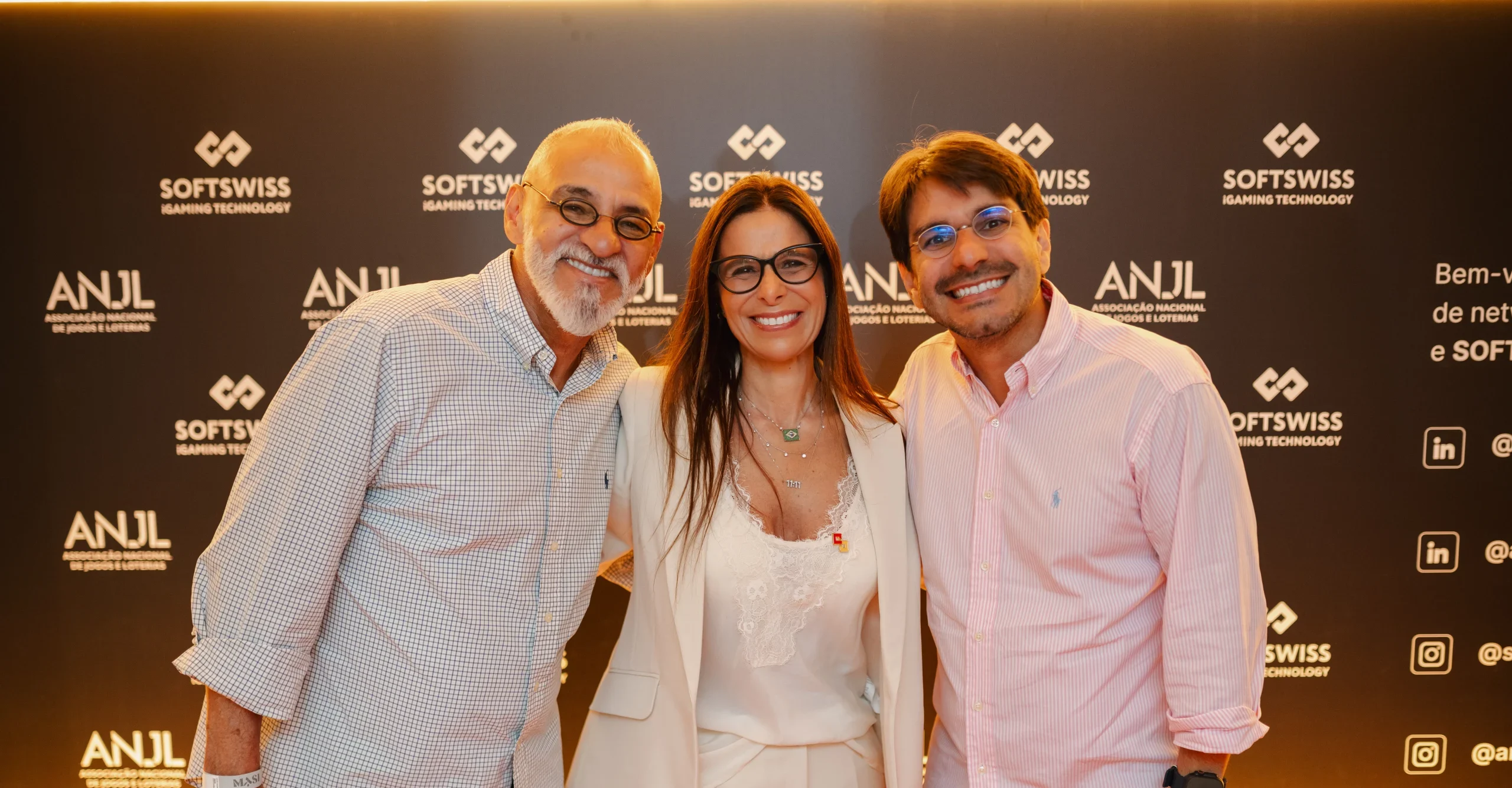 3 people smiling at the camera, SOFTSWISS gold logo in the background