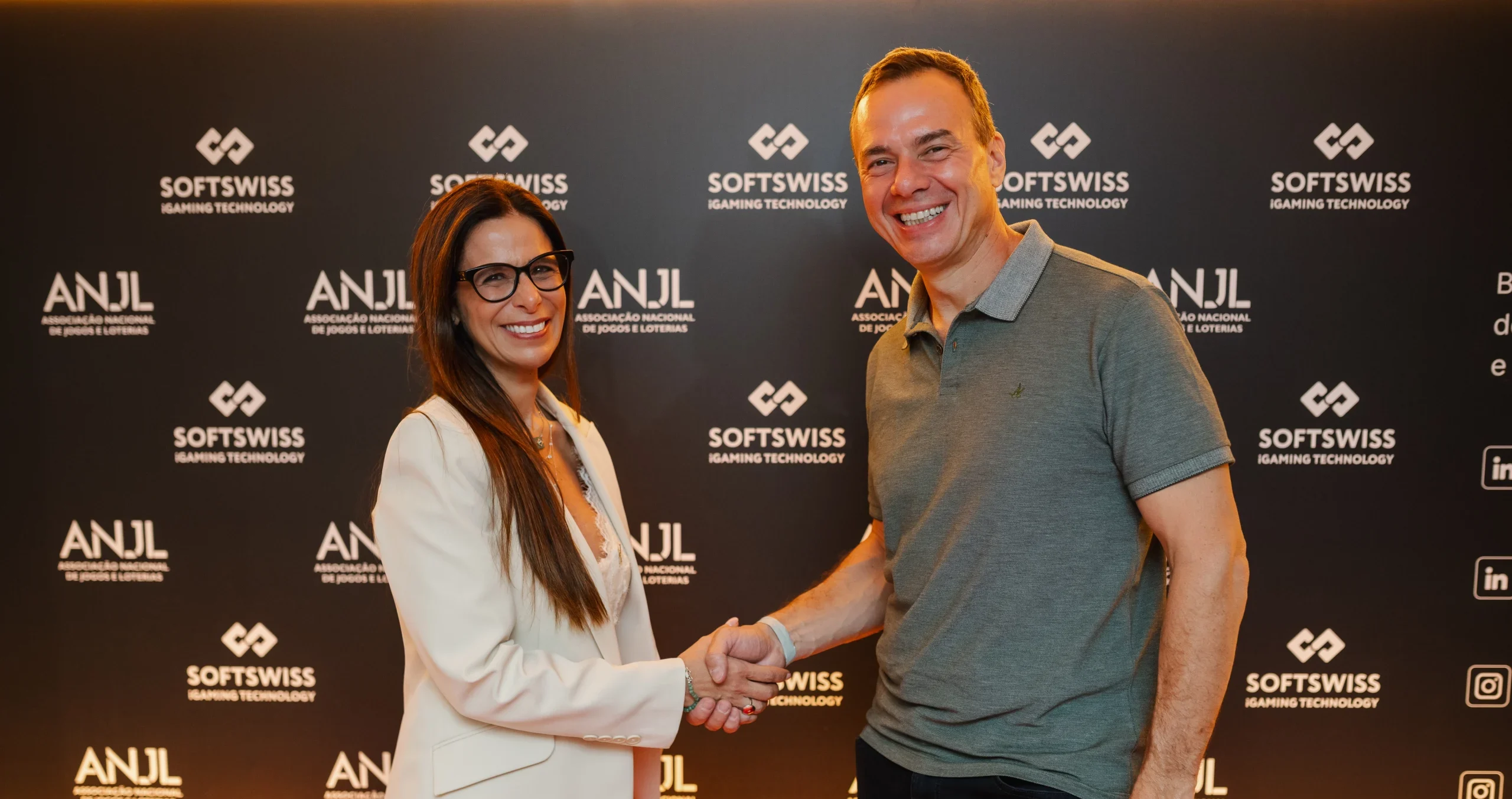 2 people shaking hands at the camera, SOFTSWISS gold logo in the background