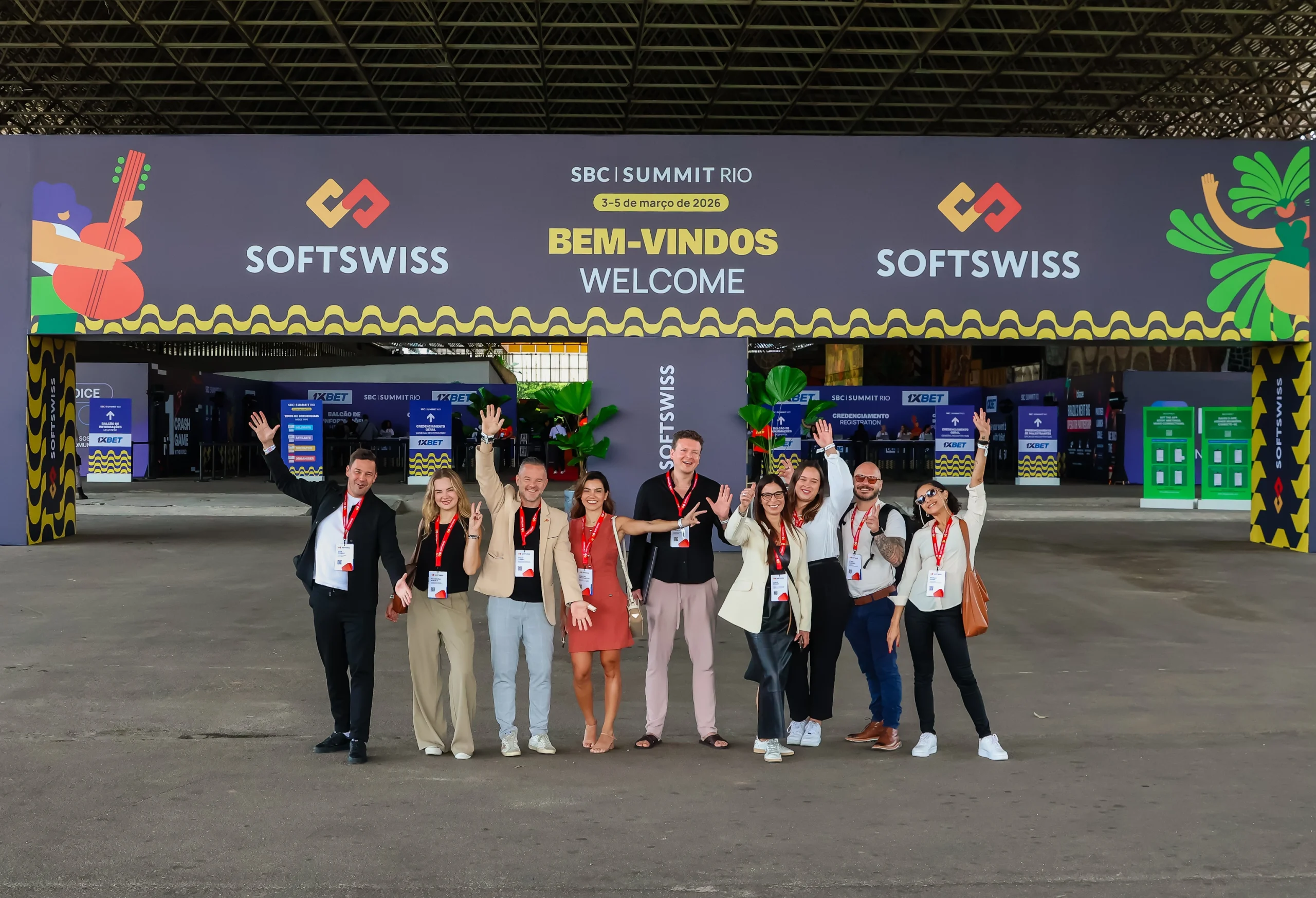 SOFTSWISS logo, ten people waving at the camera, grey floor