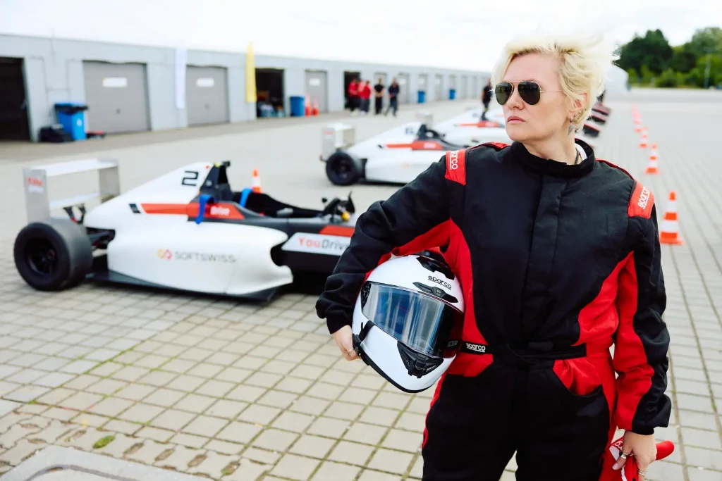 Woman in glasses with helmut, racing cars in the background